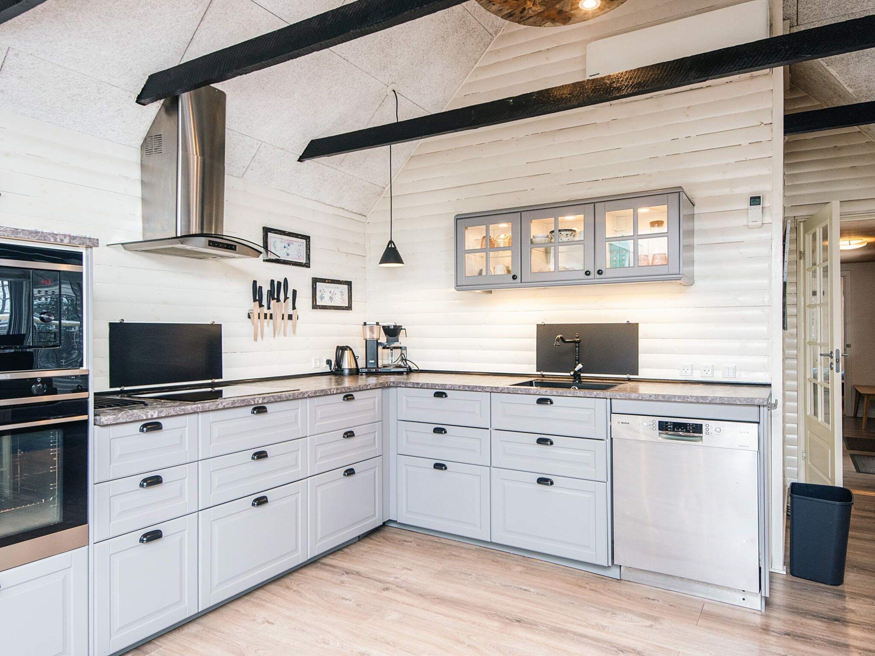 A modern kitchen with white cabinetry, a built-in oven, and a coffee machine.