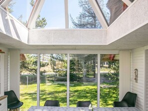 Ein sonnendurchfluteter Raum mit einer großen Glasdoor zu einem grünen Rasen, einem Tisch mit Stühlen und einem Fenster mit Blick auf Bäume.