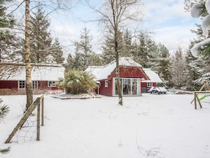 Eine rote Holzhütte mit Glastür, umgeben von schneebedeckten Bäumen und einem klaren Himmel.
