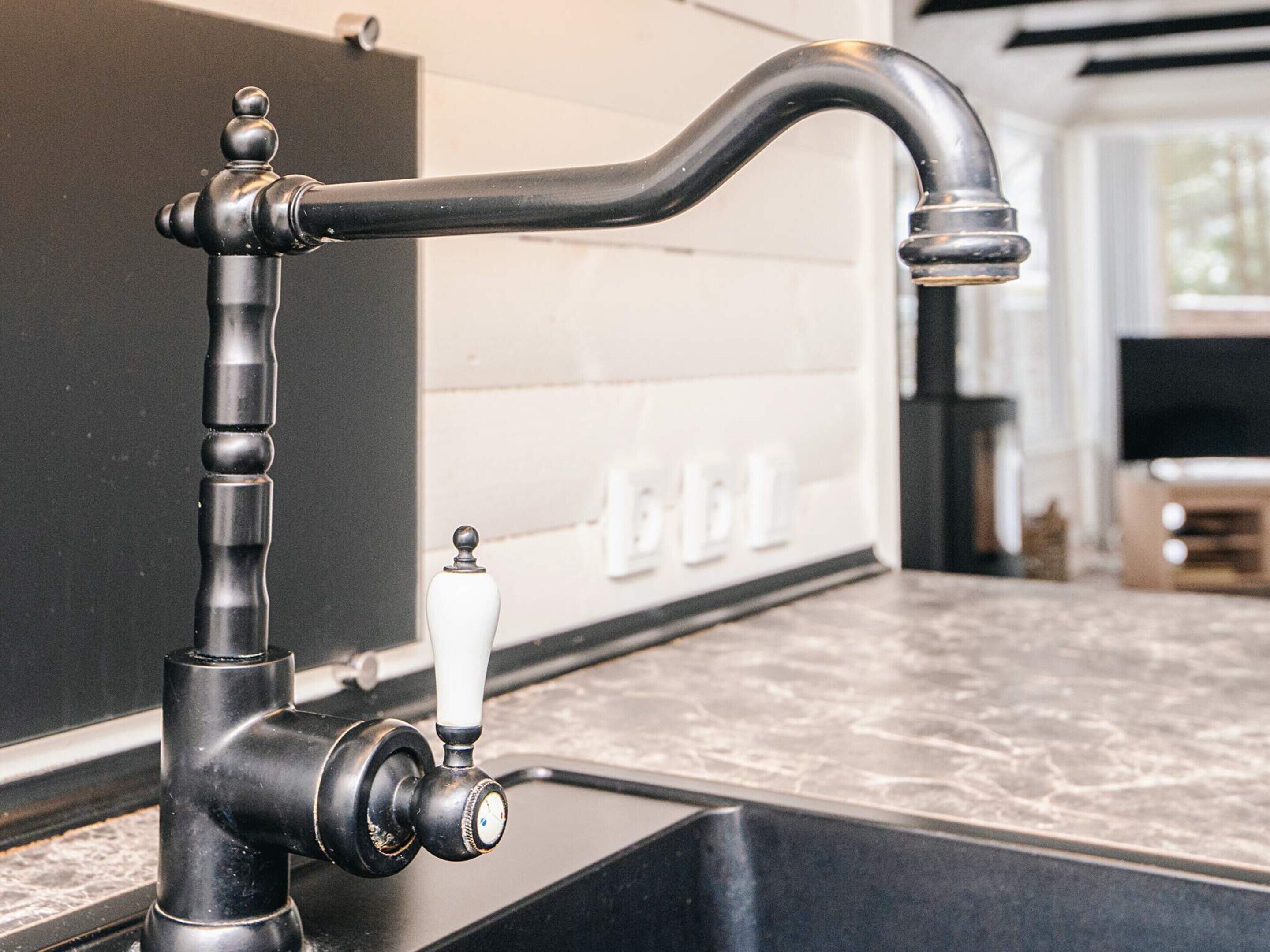 A modern kitchen with a black faucet, white tiles, and a marble countertop.