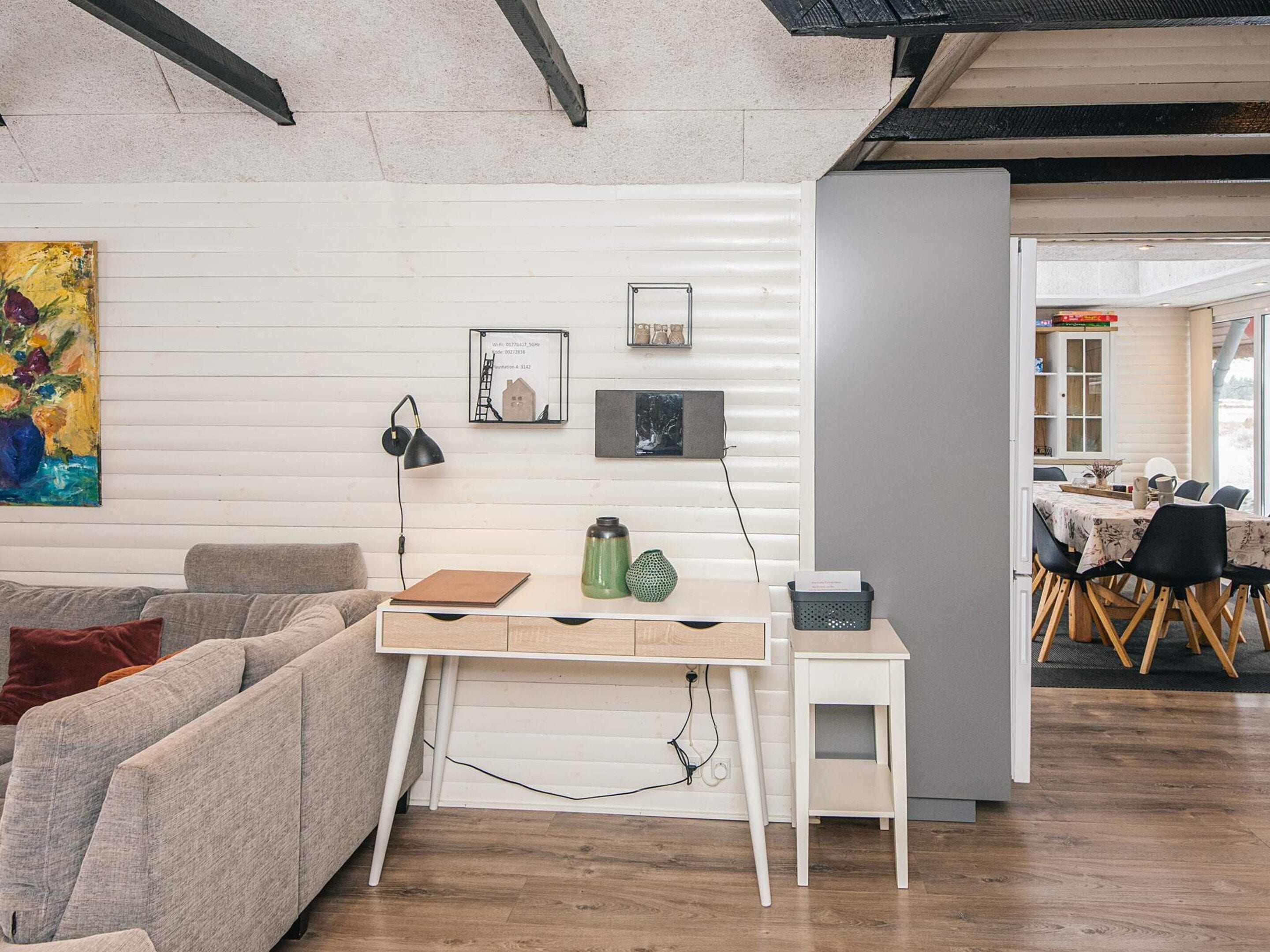 Una sala de estar moderna con una pared blanca, un sofá gris, una mesa de centro de madera y un comedor con mesa y sillas.