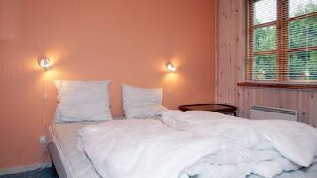 A single bed with two pillows, a bedside table, and a window with blinds.
