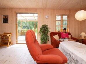 A cozy room with a wooden interior, a red armchair, a sofa, a table with a lace tablecloth, and a potted plant.