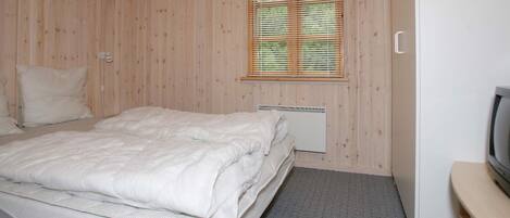 A bedroom with a bed, a window with blinds, a radiator, and a television on a stand.