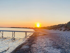 A sunset over a beach with a boardwalk leading to the water.