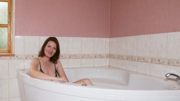 Eine Person sitzt in einer Badewanne mit Fenster und gefliesten Wänden.