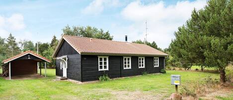 A black wooden house with a red-tiled roof, a small attached garage, and a sign indicating it is a museum.