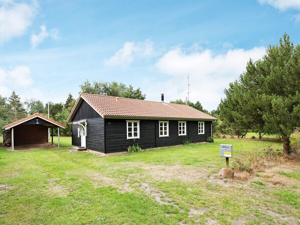 A black wooden house with a red-tiled roof, a small attached garage, and a sign indicating it is a museum.