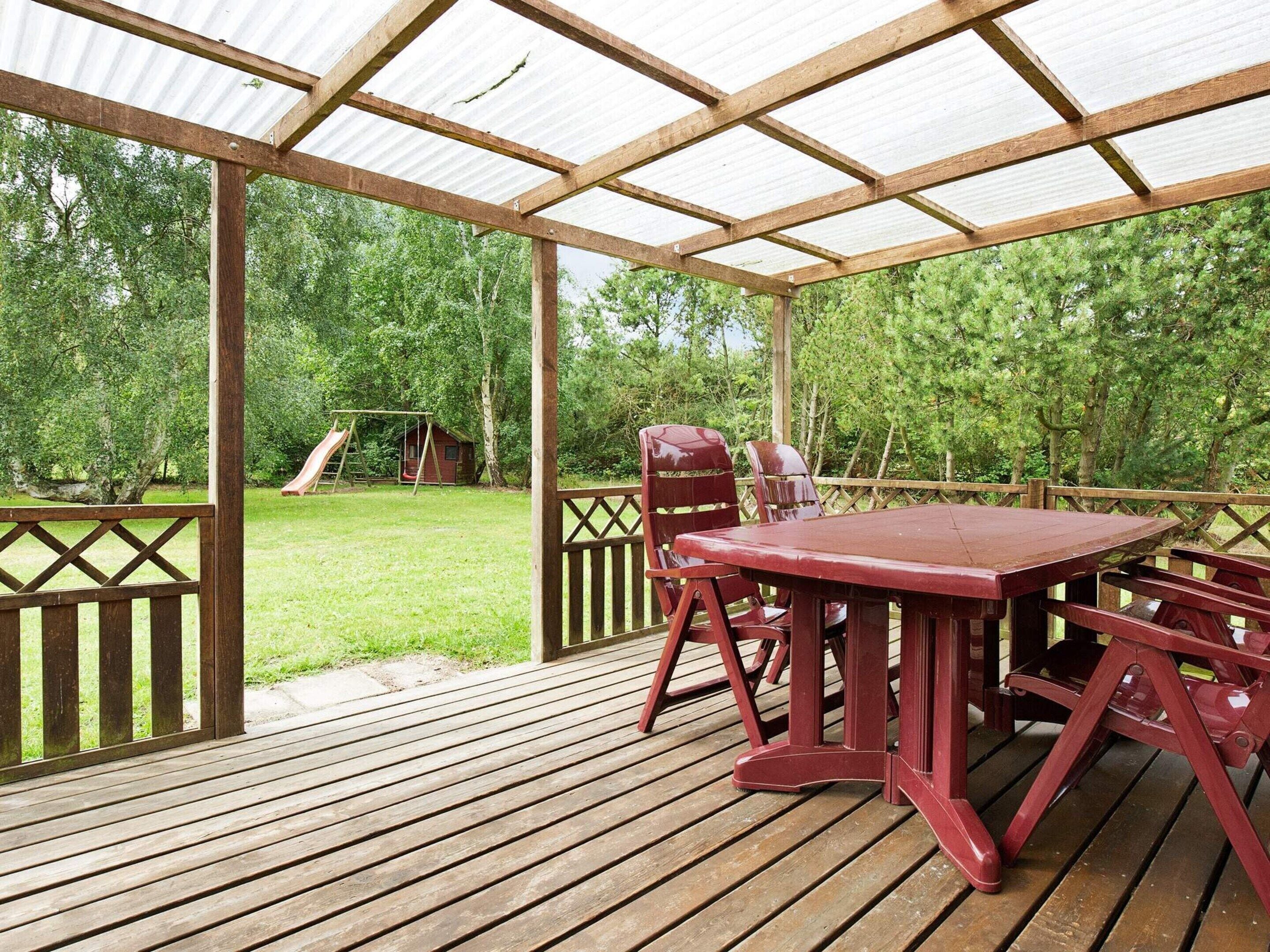 A wooden deck with a table and chairs, a swing set, and a wooden fence.
