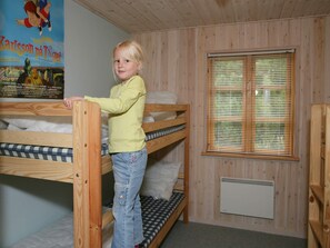 A child standing on a bunk bed in a room with wooden walls and a window with blinds.