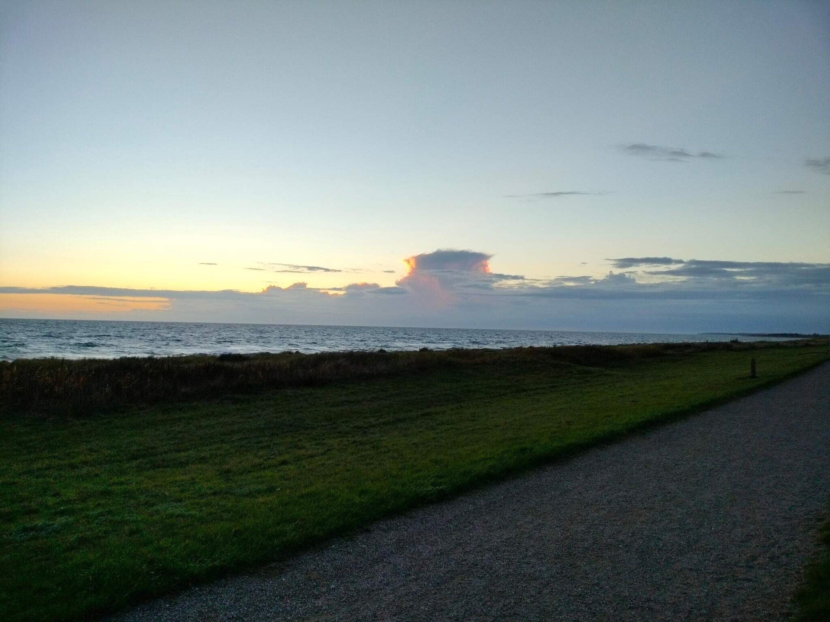 Een grindpad langs een gazon met uitzicht op zee en een zonsondergang.