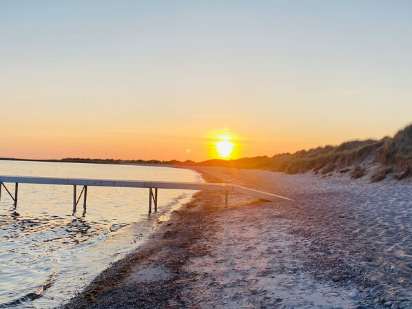 A sunset view over a beach with a wooden walkway leading to the water.