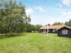A house with a porch, a flagpole, and a grassy yard. - 8 Person Holiday Home in Rodby (Rodby)