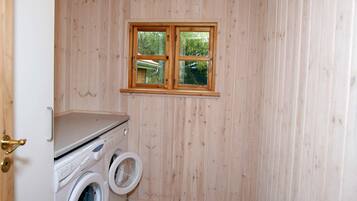 A laundry room with wooden walls, a window, and a washing machine.