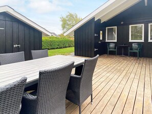 Un espace extérieur abrité, équipé d’une table et de chaises, d’une petite table avec des chaises, et offrant une vue sur une haie et le ciel.