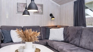 A modern living room with a grey sectional sofa, a white coffee table with a vase of dried plants, and two black pendant lights. - 4 Star Holiday Home in Hemmet (Hemmet)