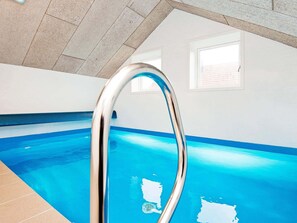 Une piscine avec un escalier en métal, des murs carrelés et un plafond en pente.