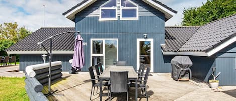 A two-story building with a patio area featuring a table and chairs, a barbecue grill, and a wooden deck.
