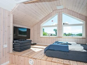 Quarto aconchegante com teto inclinado, televisão, cama e janelas amplas com vista para o exterior.