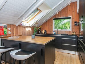 Cozinha moderna com interior de madeira, uma ilha grande, banquetas de bar e vista para o verde lá fora.