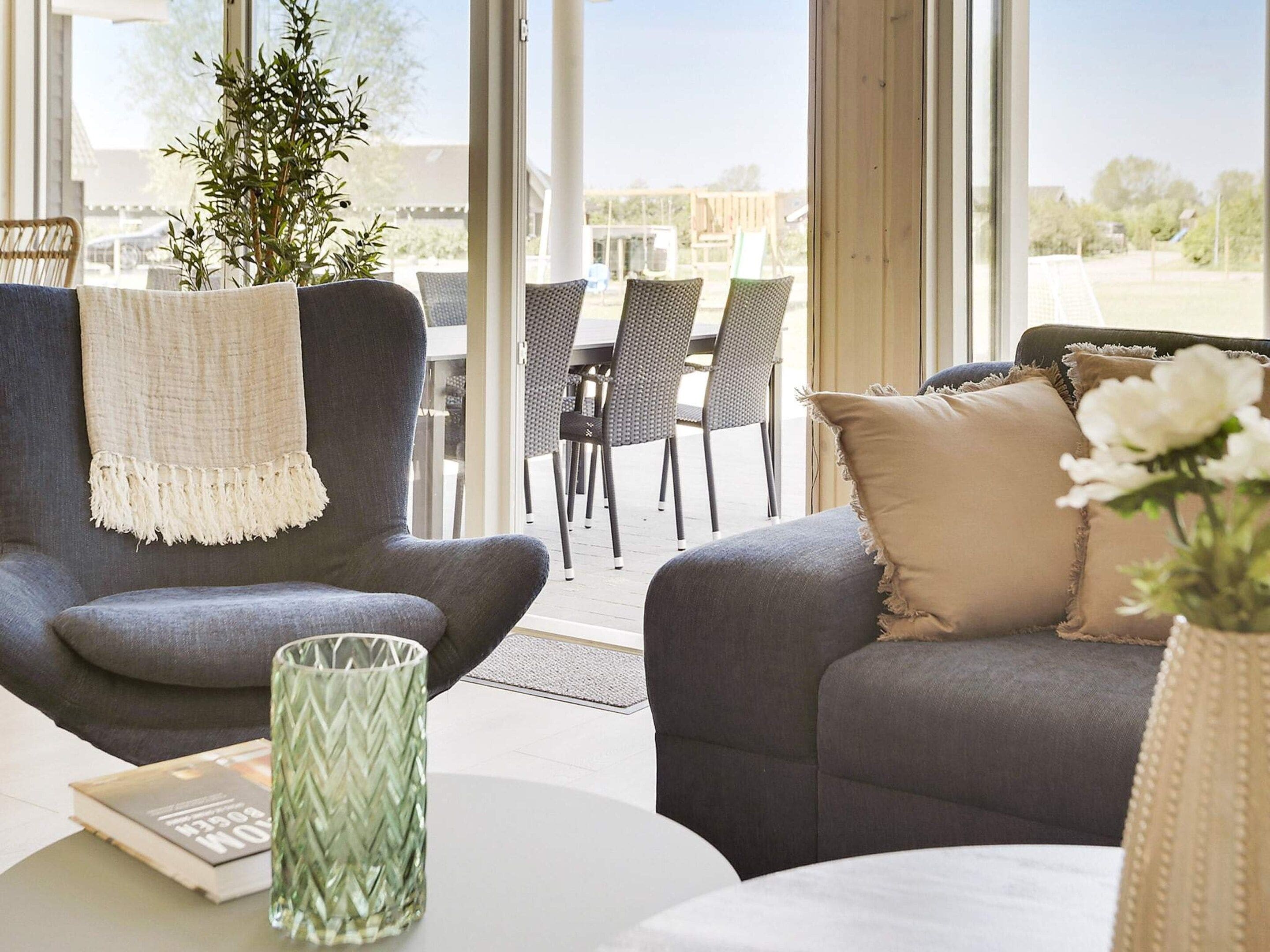 A modern living room with a grey sofa, a matching armchair, and a dining area with wicker chairs.