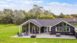 A modern building with large windows, a covered patio, and a grassy area with outdoor seating. - 5 Star Holiday Home in Idestrup (Idestrup)