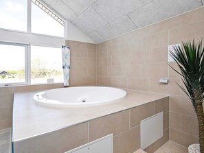 Une salle de bain avec une grande baignoire, une fenêtre et une plante en pot.