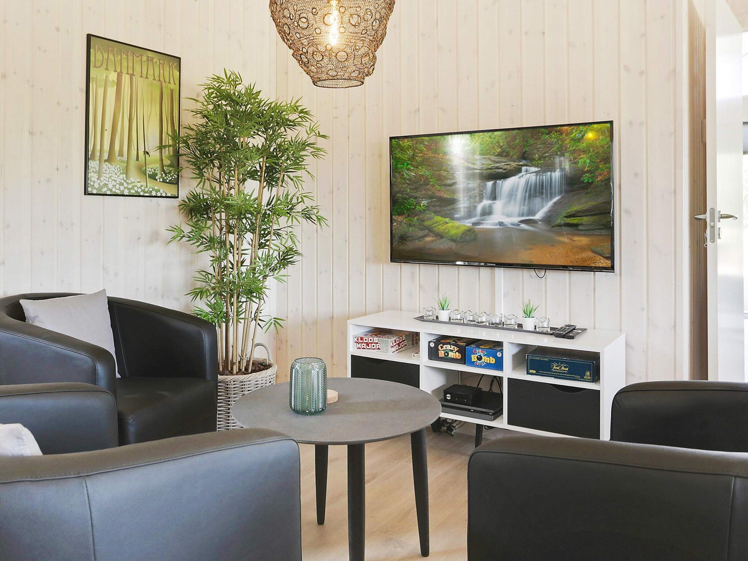 A living room with a sofa, a coffee table, a TV, a plant, and a wall-mounted shelf with decorative items.