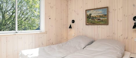 A bedroom with a bed, a window, a painting, and a wall-mounted lamp.