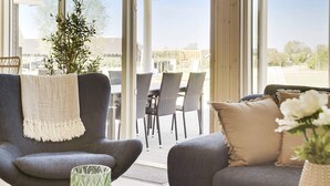 A modern living room with a grey sofa, a matching armchair, and a dining area with wicker chairs. - 5 Star Holiday Home in Idestrup (Idestrup)