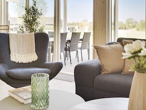 A modern living room with a grey sofa, a matching armchair, and a dining area with wicker chairs.