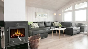 A modern living room with a wood-burning stove, a grey sofa set, a small round table, and large windows.