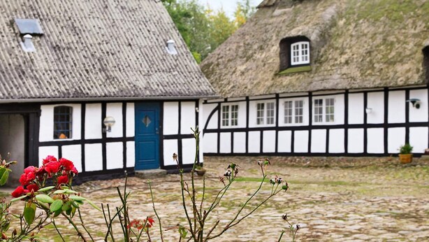 Il s’agit d’un bâtiment traditionnel, doté d’un toit de chaume et de murs blancs, avec une porte bleue et de nombreuses fenêtres.