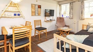 Un salon chaleureux avec un plafond en bois, un téléviseur fixé au mur, un coin repas avec une table et des chaises en bois, et une fenêtre avec des rideaux.