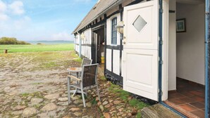 Une maison traditionnelle avec une cour dallée de pierres, une chaise à l’extérieur et une vue sur la mer.