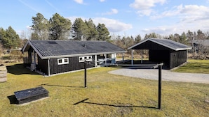 A rustic cabin with a metal roof, a covered outdoor area, and a small deck. - 4 Star Holiday Home in Blokhus (Blokhus)