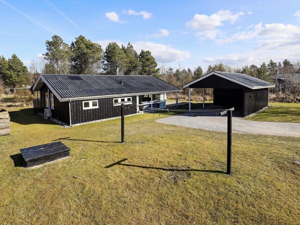 A rustic cabin with a metal roof, a covered outdoor area, and a small deck. - 4 Star Holiday Home in Blokhus (Blokhus)