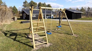 A wooden swing set in a grassy yard with a metal roof structure in the background. - 4 Star Holiday Home in Blokhus (Blokhus)