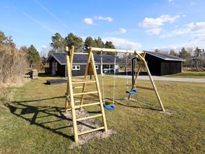 A wooden swing set in a grassy yard with a metal roof structure in the background.