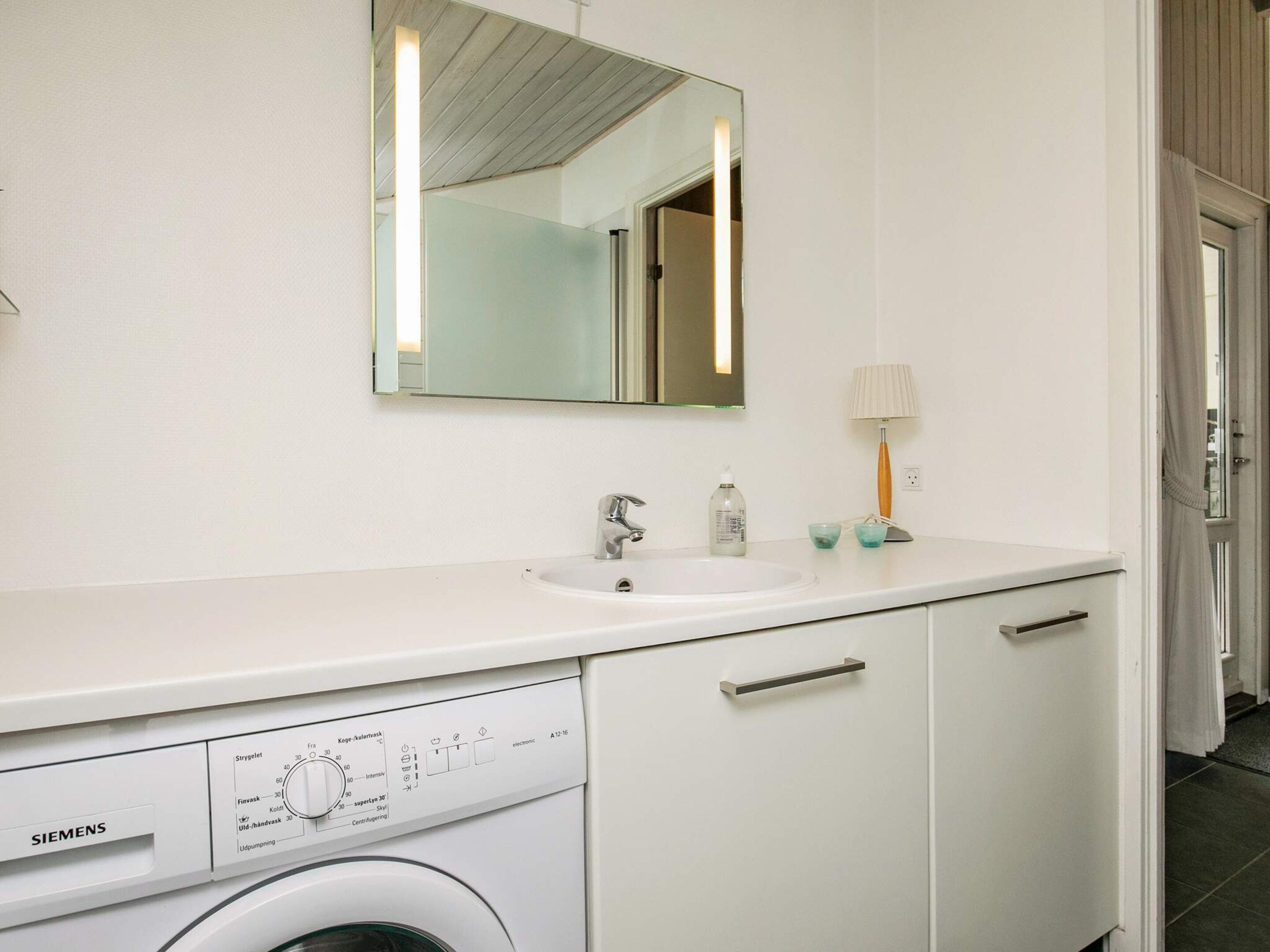 A modern bathroom with a white sink, mirror, and a Siemens washing machine.