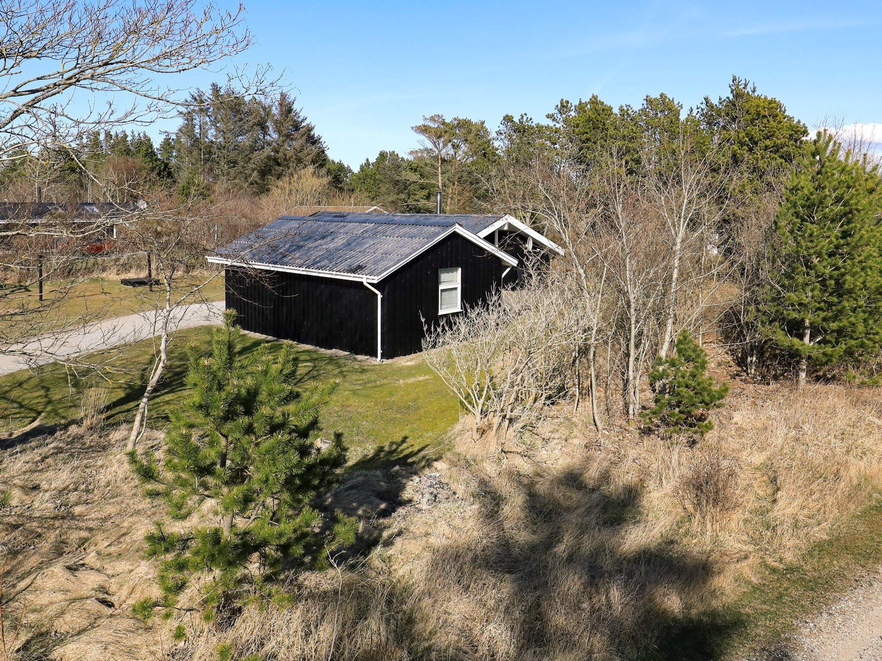 A black metal shed with a sloped roof, surrounded by trees and grass.