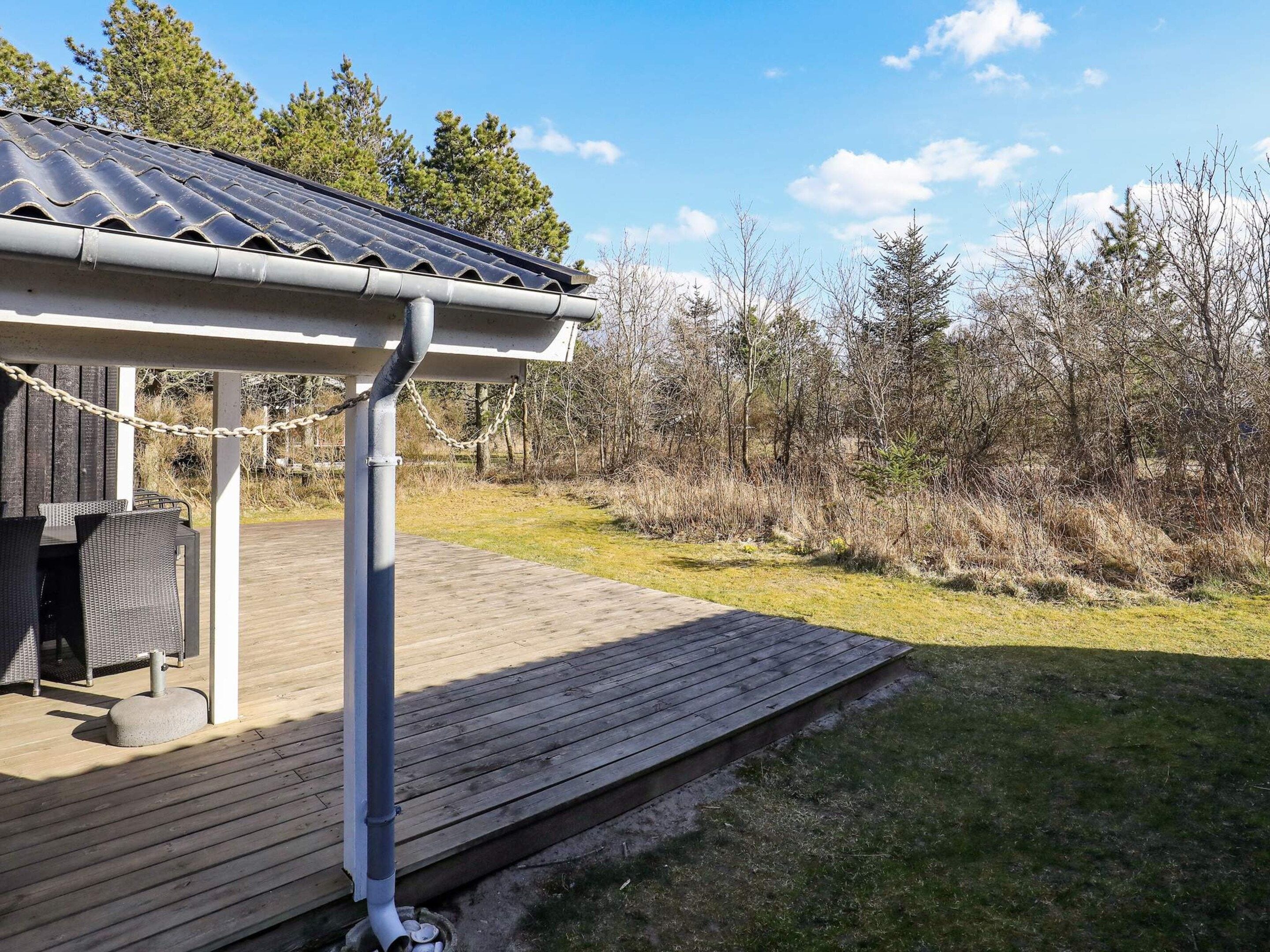 A wooden deck with a covered seating area, a metal gutter, and a natural landscape with trees and grass.