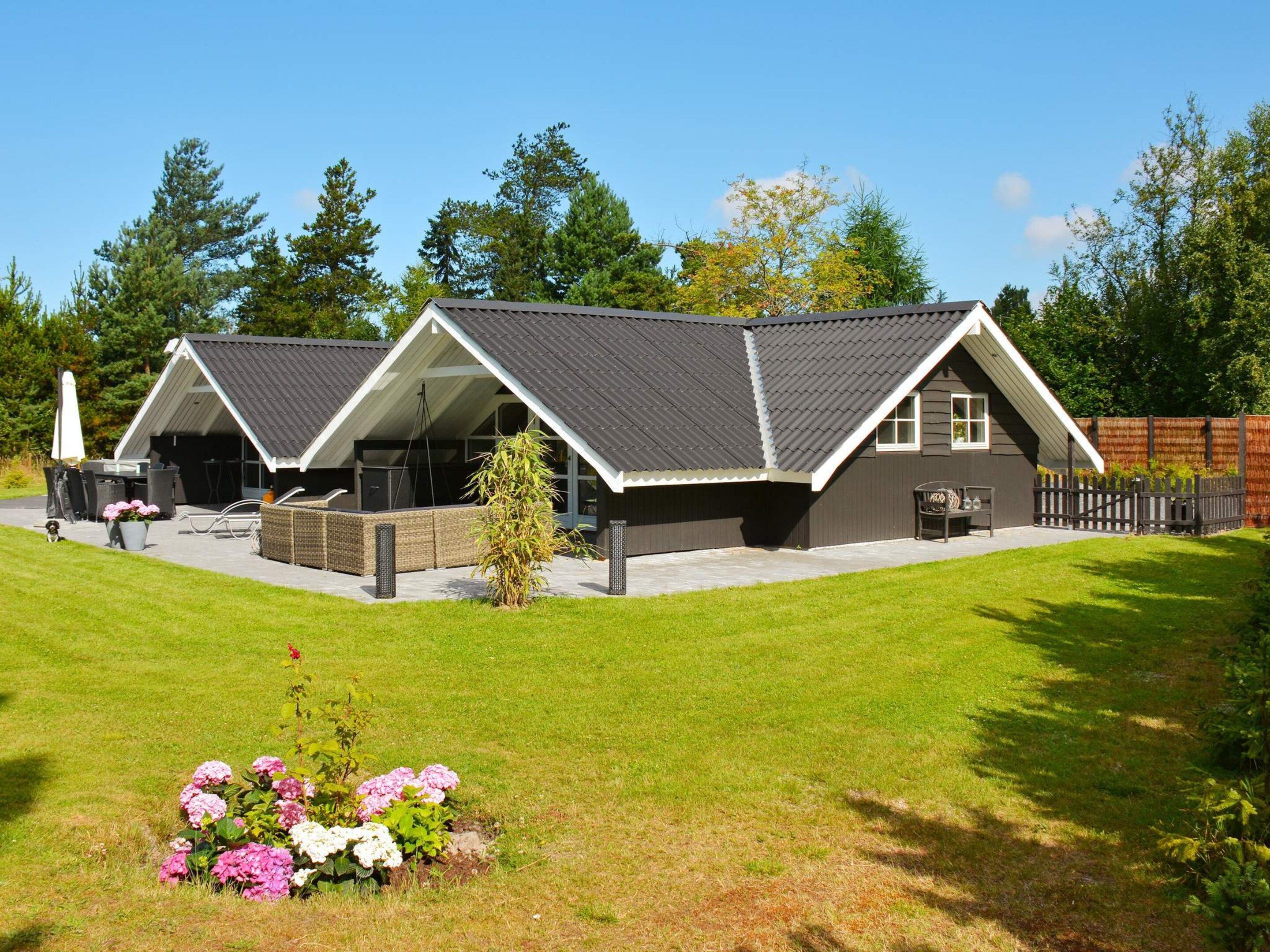 A modern two-story house with a sloped roof, a covered patio, and a fenced backyard.