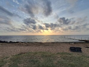 Une plage avec une jetée en bois qui s’avance dans l’eau, un rivage sablonneux et un ciel nuageux.
