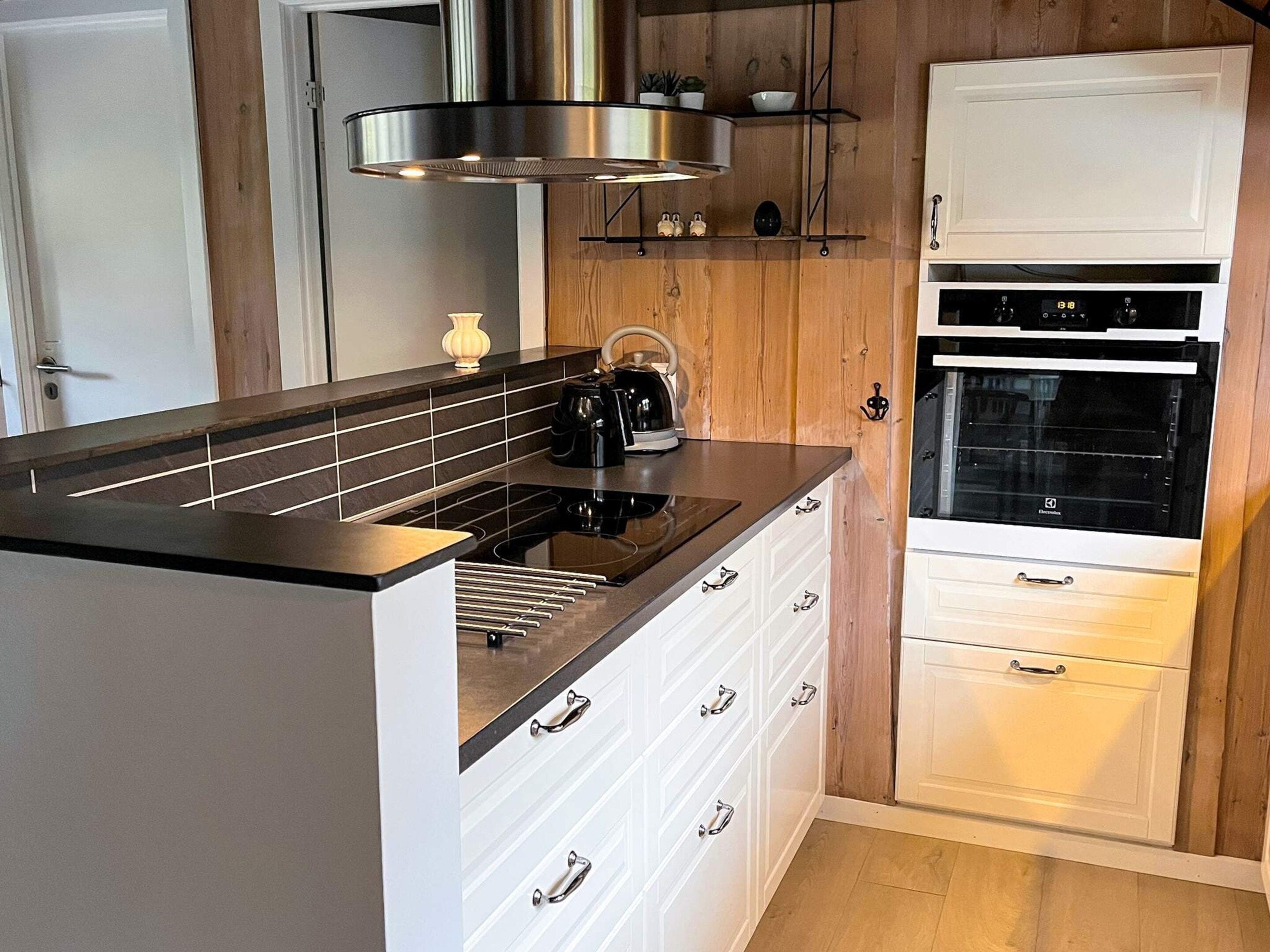 A modern kitchen with a black countertop, stainless steel range hood, white cabinetry, and a built-in oven.