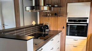 A modern kitchen with a black countertop, stainless steel range hood, white cabinetry, and a built-in oven.