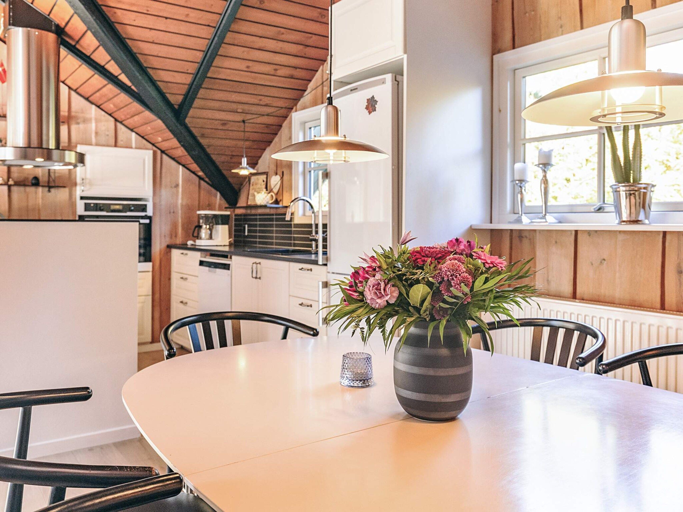 A modern kitchen with wooden cabinets, a dining table with chairs, and a vase of flowers.