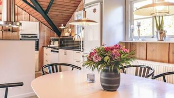 A modern kitchen with wooden cabinets, a dining table with chairs, and a vase of flowers.