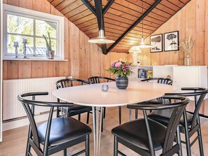 Een eethoek met een ronde tafel, zwarte stoelen en een bloevas. Er is een raam met planten en kaarsen op de vensterbank.