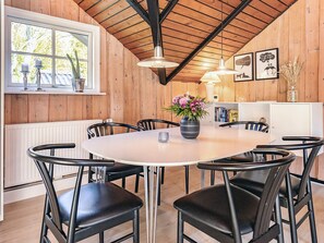 Un coin repas avec une table ronde, des chaises noires, un vase de fleurs et des murs en bois.